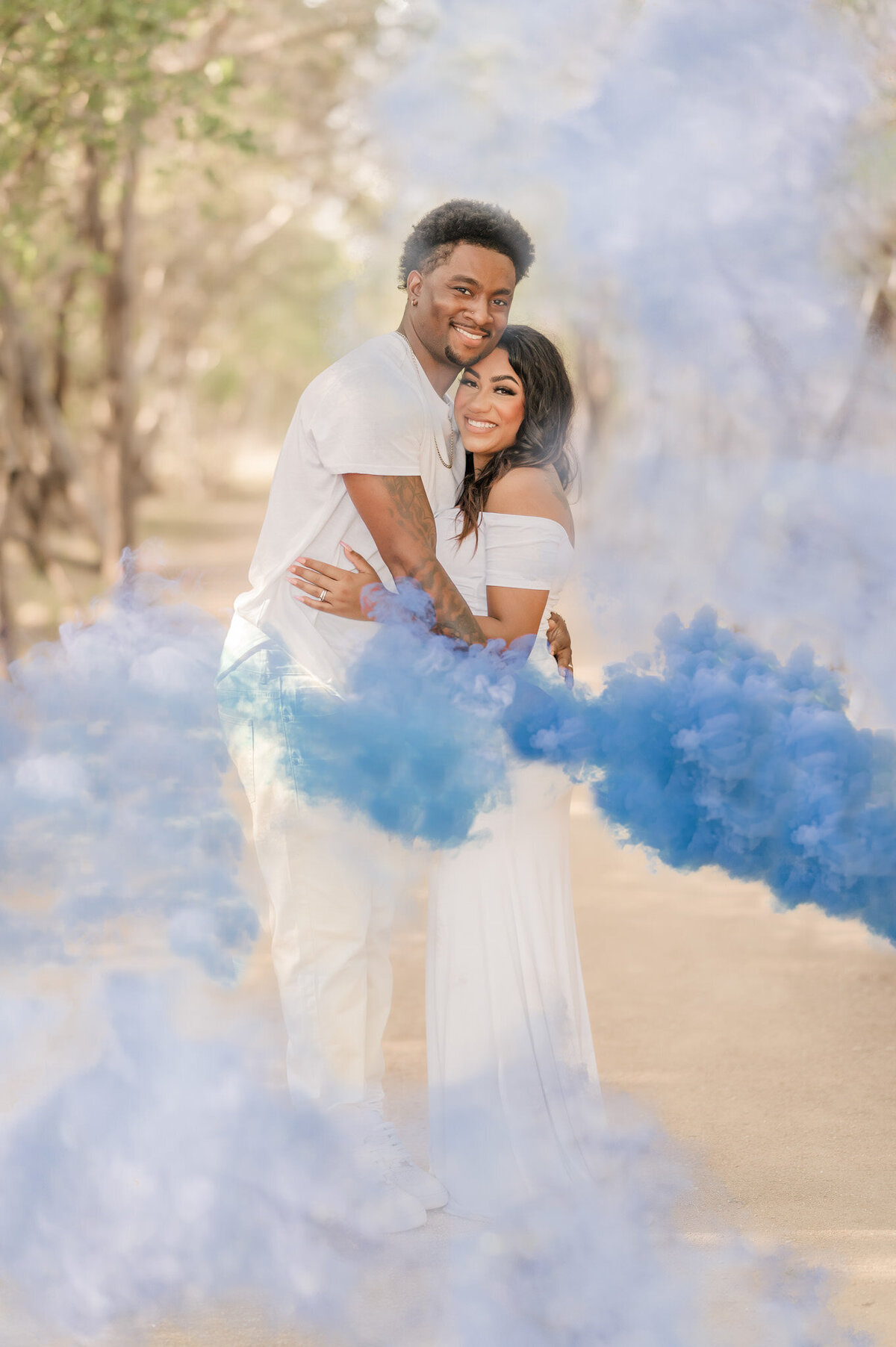 Pregnant San Antonio couple hugs surrounded by blue smoke after a gender reveal with Cassey Golden Photography.