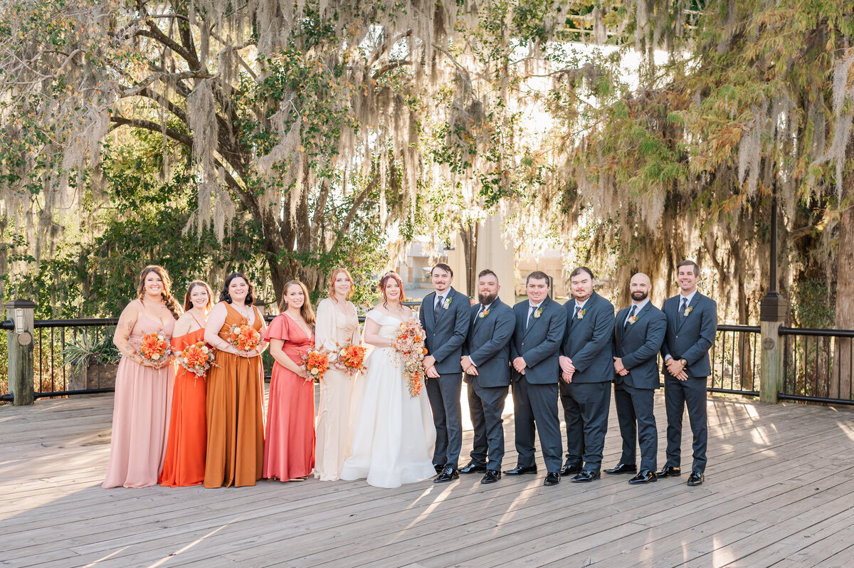 A beautiful wedding party with a bride and a groom on the riverwalk in Conway South Carolina at sunset in the fall by JoLynn Photography, a Raleigh wedding photographer