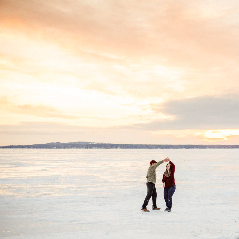 frozen gull lake in the winter couple dances over lice and sunset