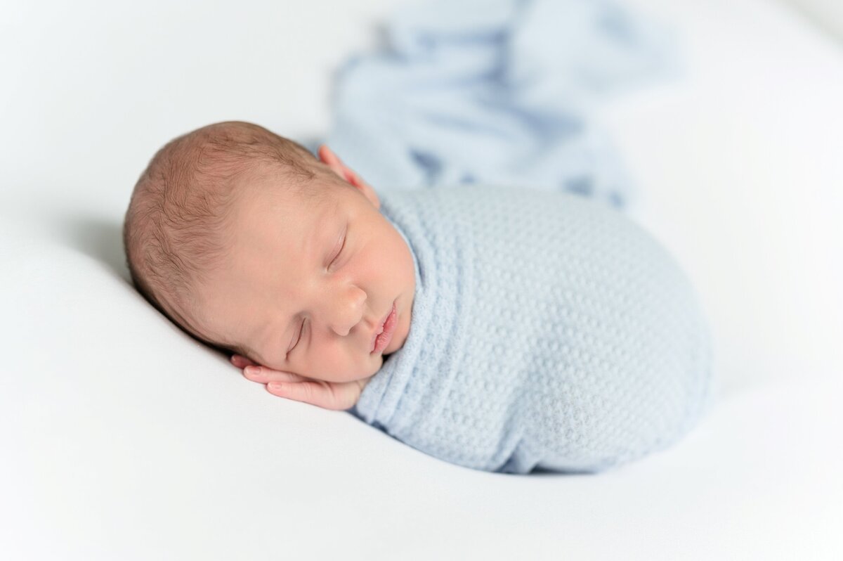 Newborn swaddled in a pastel wrap laying on his tummy in a studio.