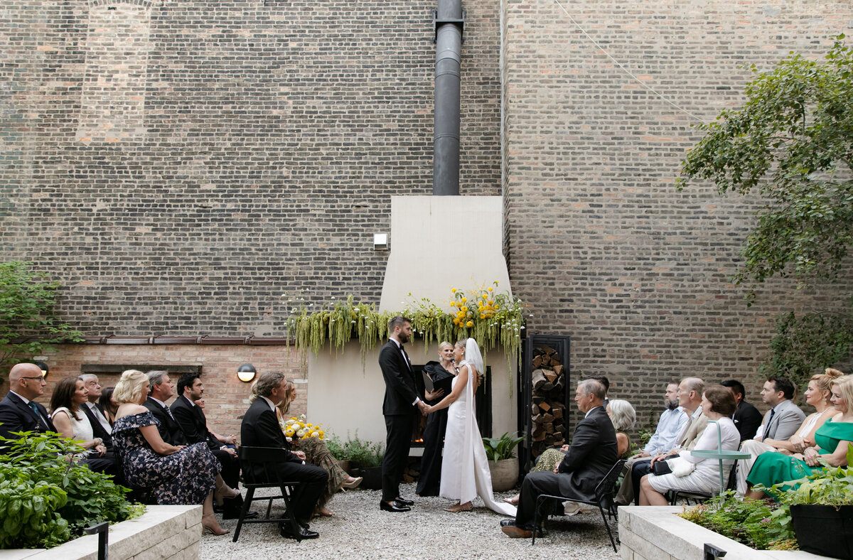 Minimalist bride and groom stand hand-in-hand exchanging vows in front of friends and family at a gorgeous Chicago  wedding ceremony.