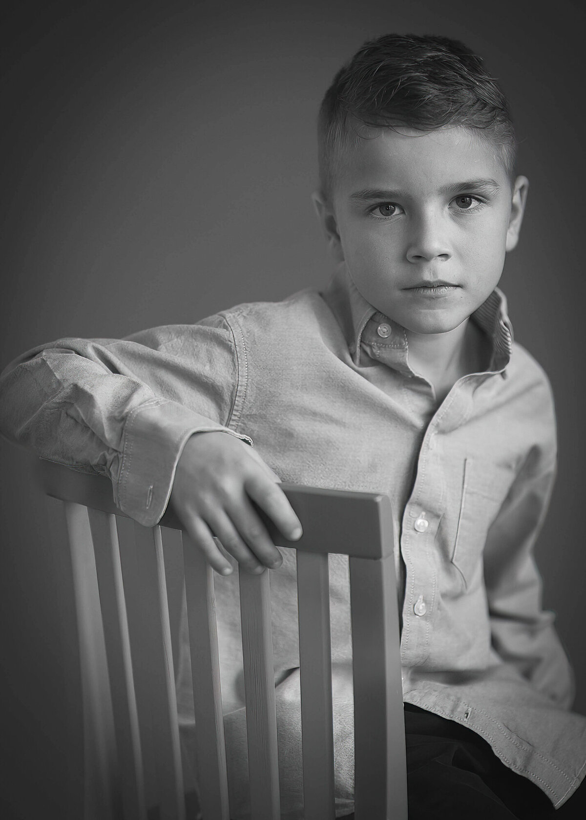 black and white portrait of serious young boy sitting in chair