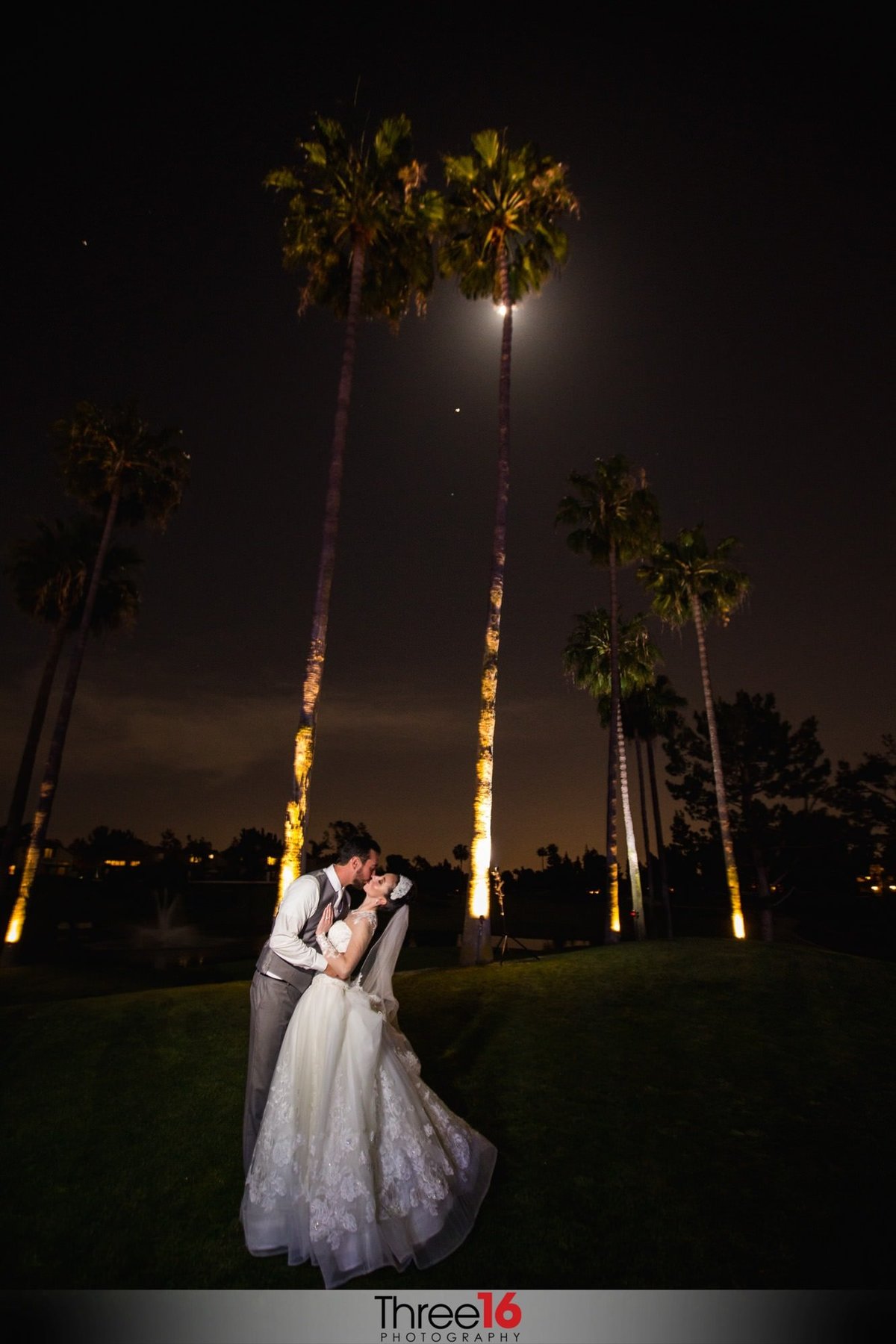 Bride and Groom kiss during the night in front of lighted palm trees