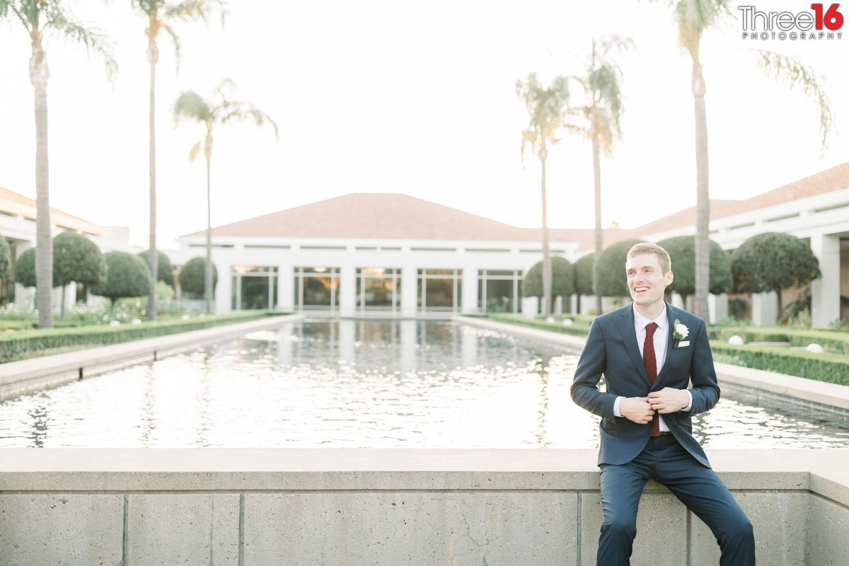Groom adjusts his coat while sitting on the reflecting pool wall at the Richard Nixon Library