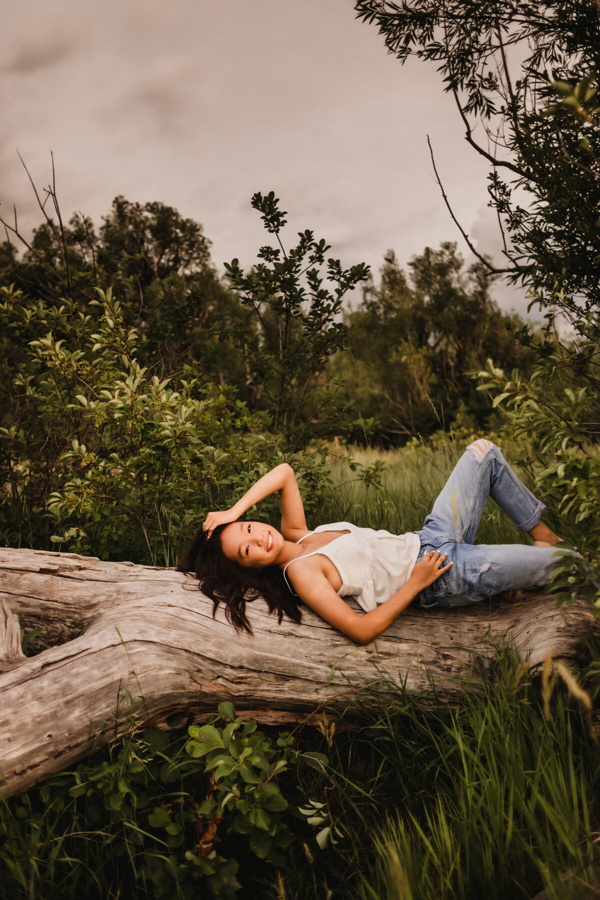 girl lays on her back on a tree stump in boulder colorado for senior photos