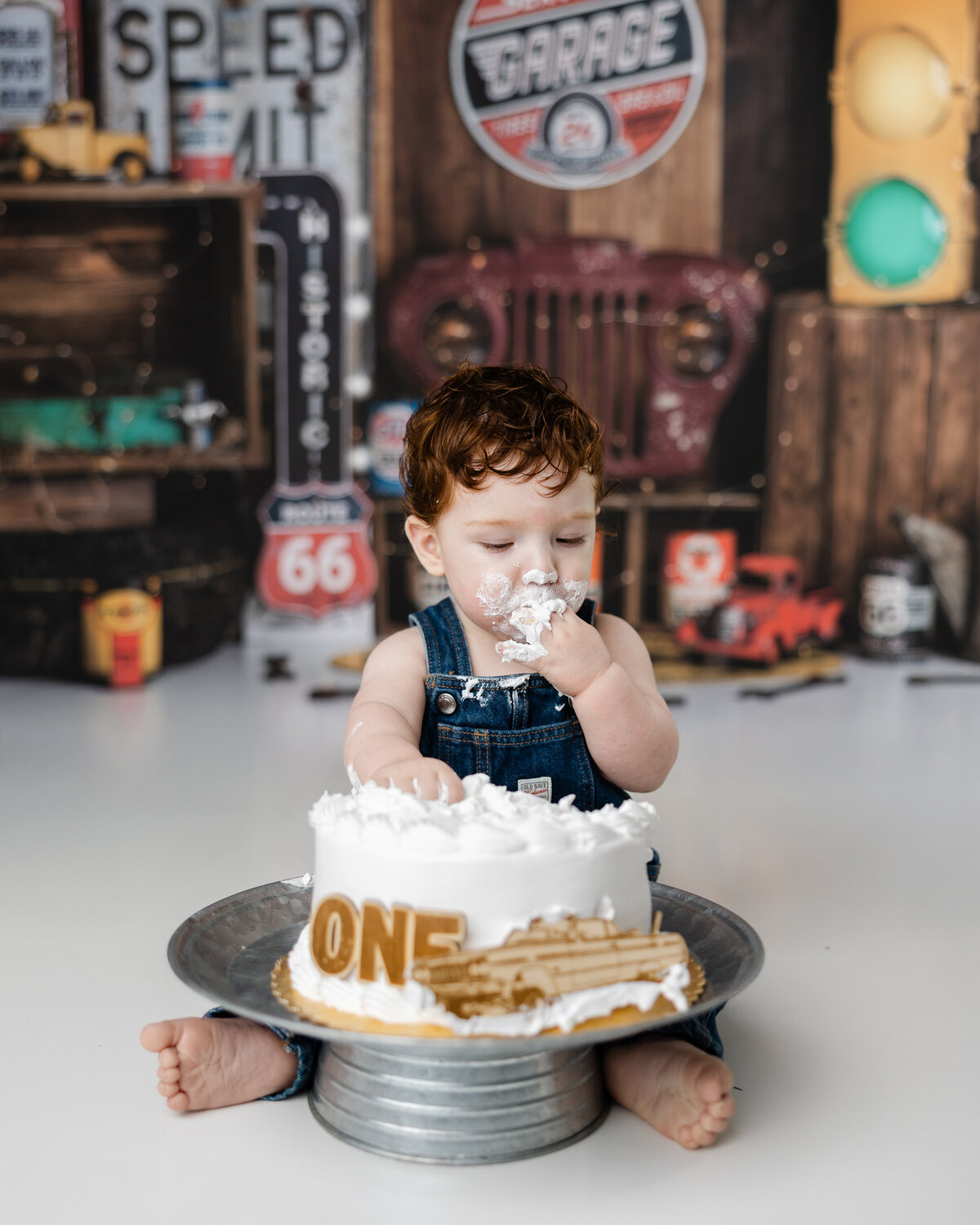 Smash cake moment with a one-year-old boy enthusiastically tasting his cake in front of Route 66-inspired decorations. Photograph by Yucaipa cake smash photographer Kaitlyn Dawn Photography.