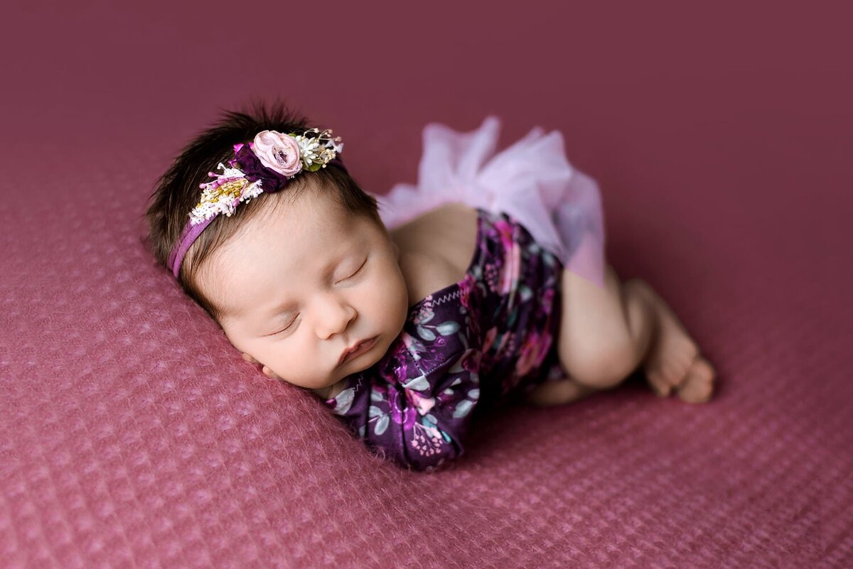 Baby photoshoot in Surrey of newborn girl in side laying pose on a mauve textured blanket