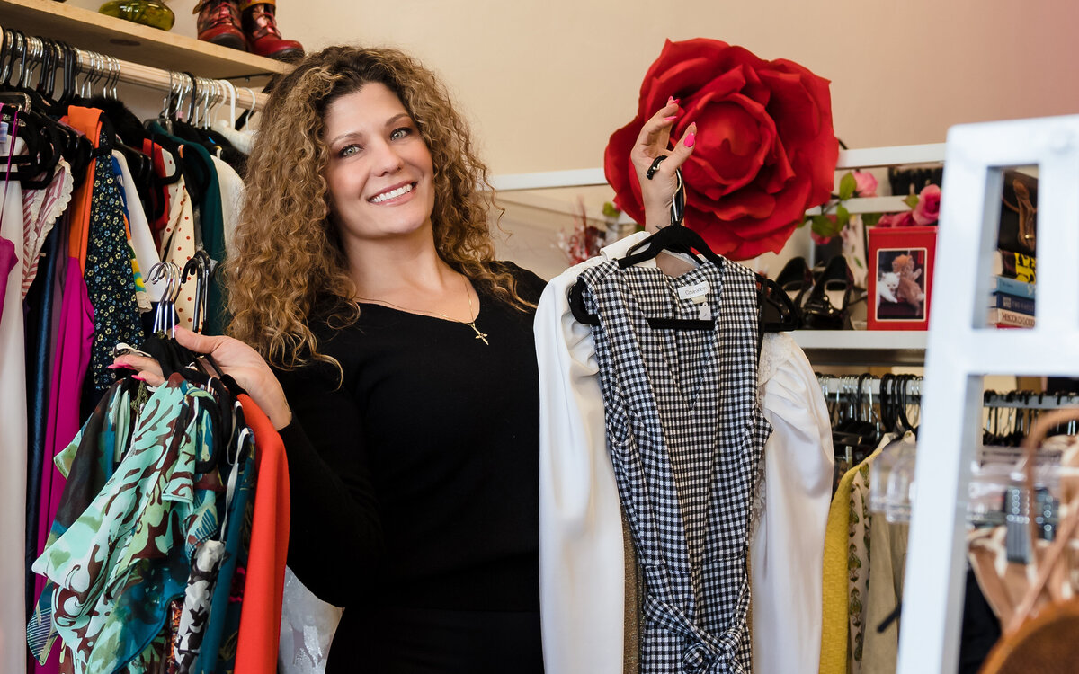 Thrift shop owner holds hangs full of clothing from her boutique