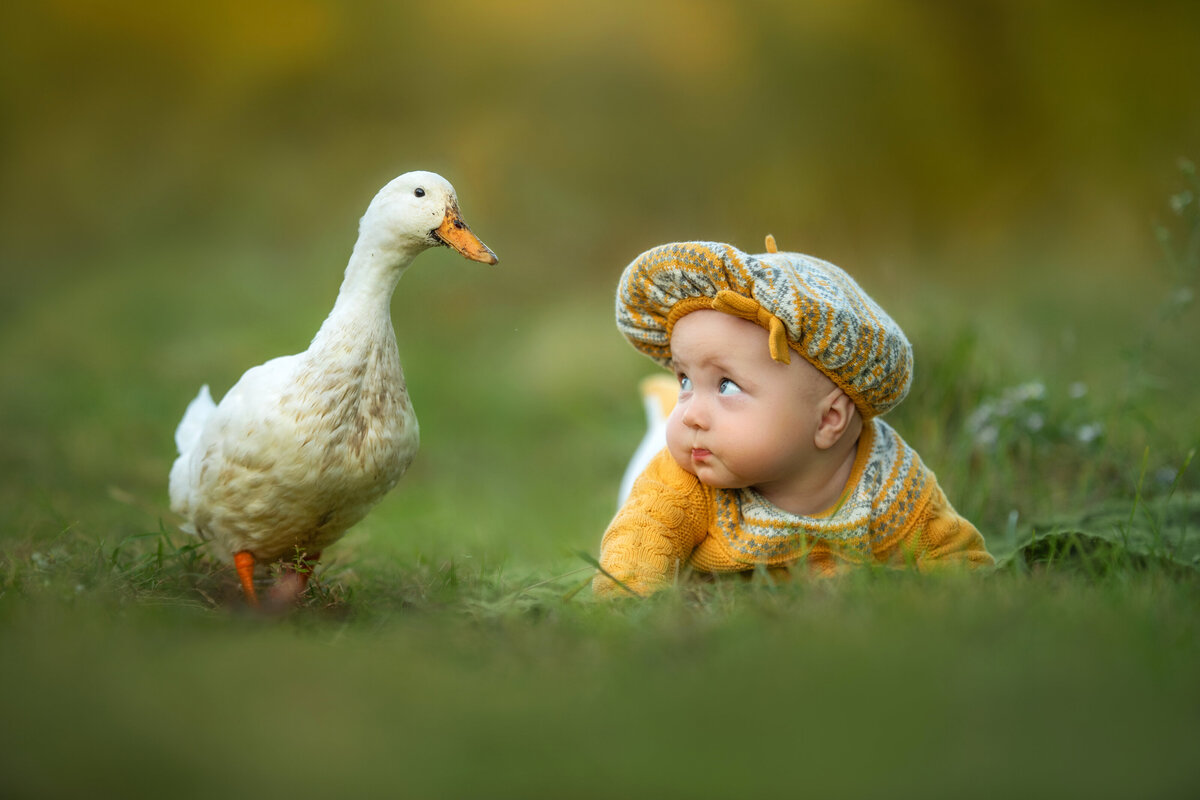 Baby girl in knitted yellow outfit from TJ Maxx and beret is having conversation with a duck from the lake in the fall.