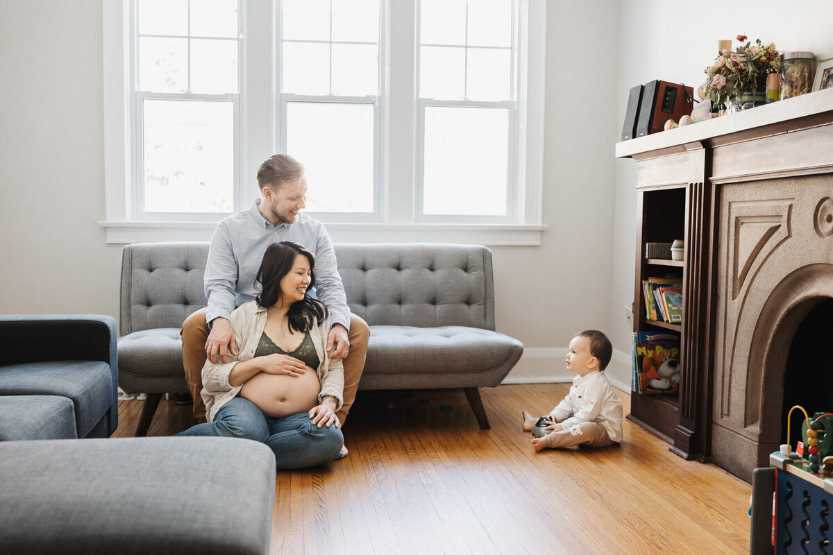 Expecting couple in their living room with their toddler son