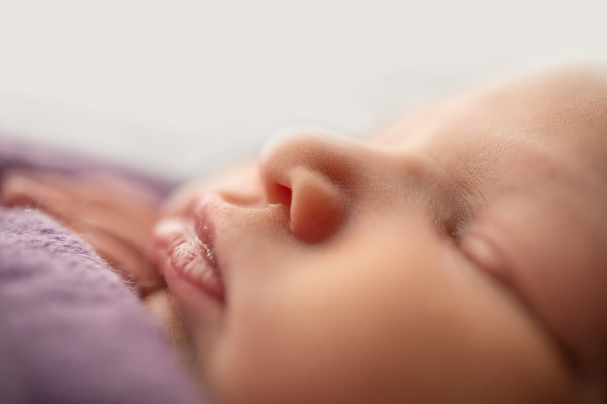 Very close up portrait of an infant's profile while sleeping. Baby's eyes, nose and mouth are shown against a white background.