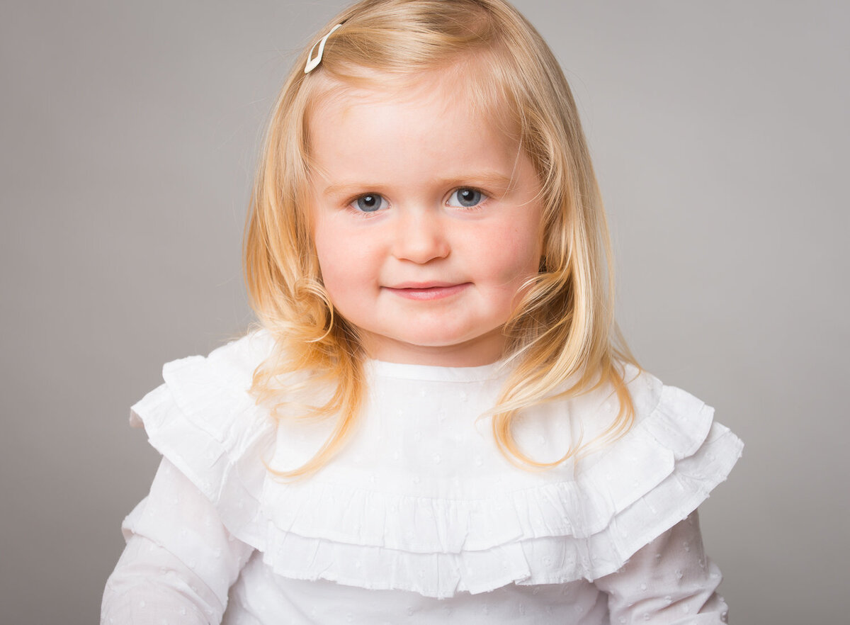 photo of a toddler with blonde hair and white top smiling