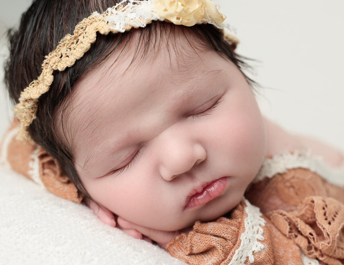 Close-up of a newborn girl with a soft headband, highlighting her sweet expression in a cozy Rochester photography studio.