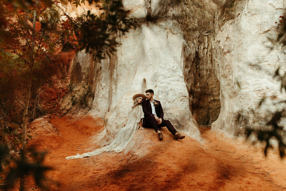 Boho bride and groom sitting back to back on a rock with white cliffs behind them and fall foliage surrounding them