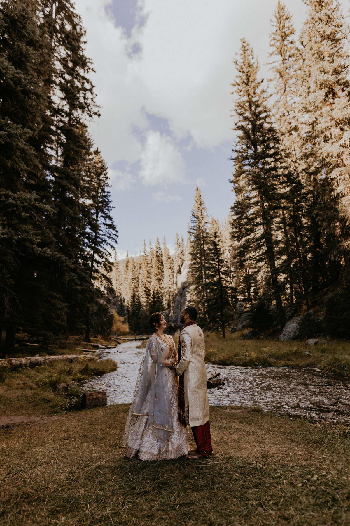 bride and groom in Indian attire holding each other in front of a creek in NM
