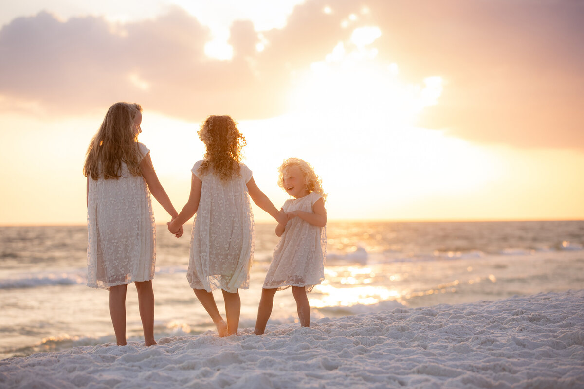 Three kids holding hands and walking at the beach at sunset