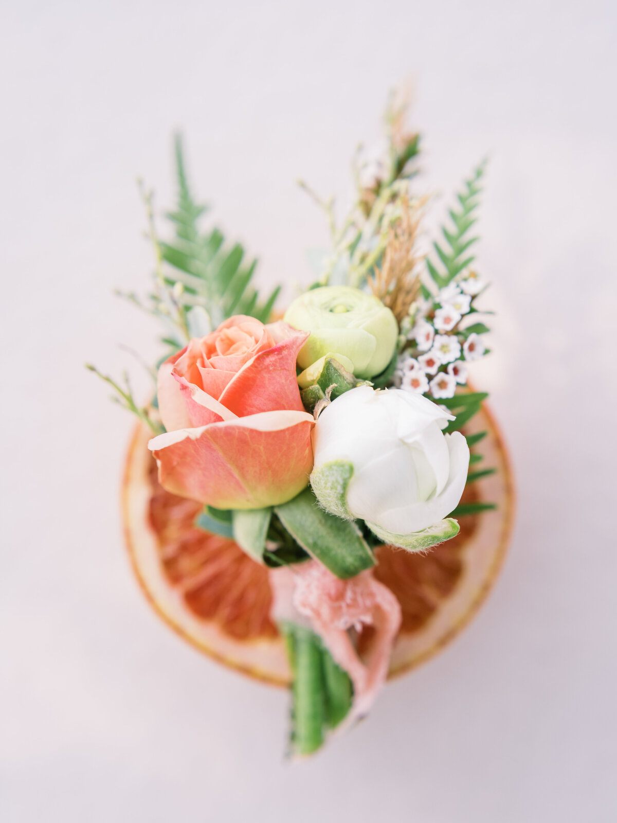 A small but mighty bouquet sitting stop half a large grapefruit matching the color palette of the wedding.