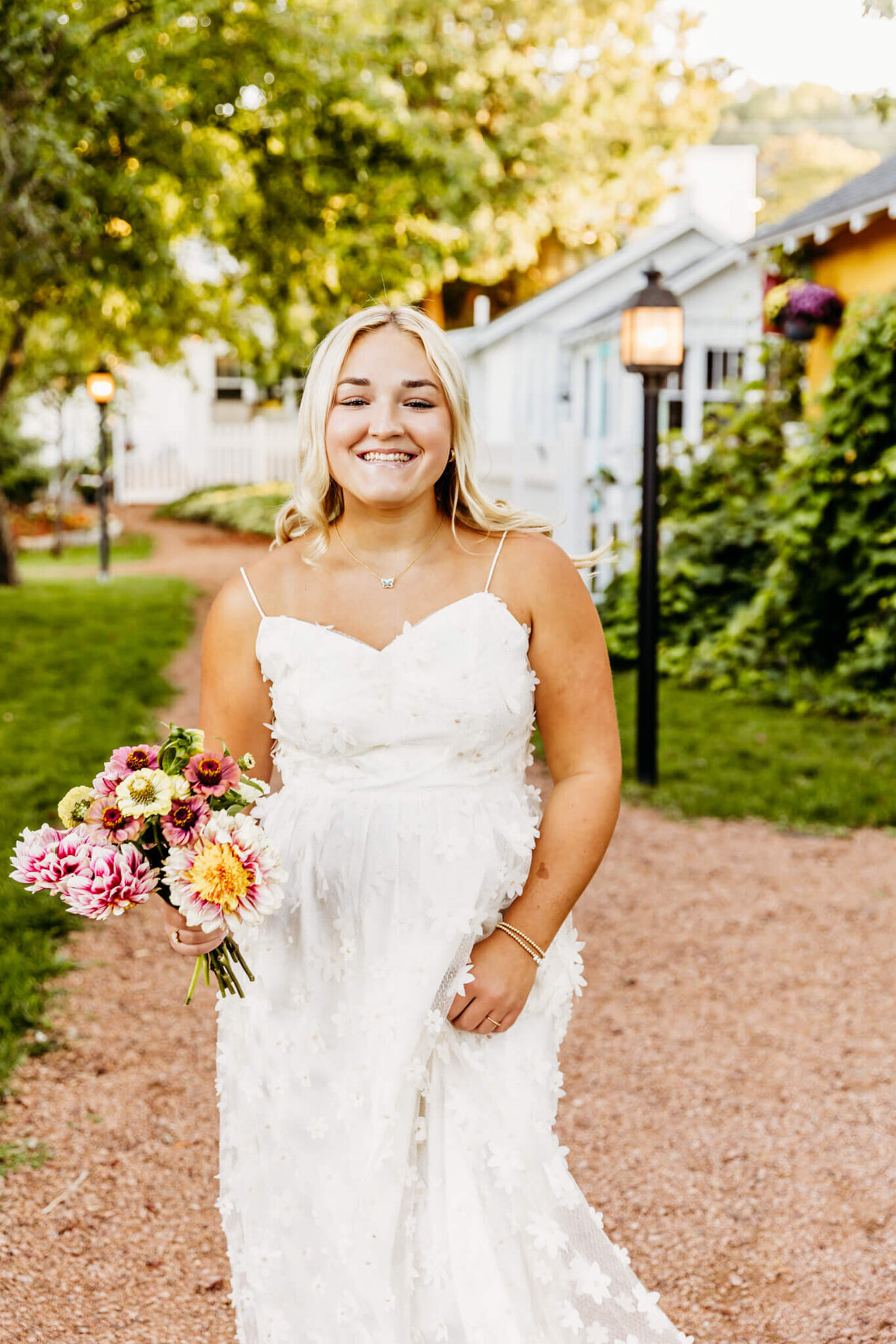 pretty high school girl in a long white flower dress holding a bouquet as she walks down a red stone pathway in Door County for her Green Bay senior photography session