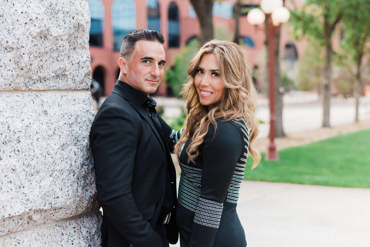 An attractive couple stand together against a white stone building downtown and smile at Northern Virginia family photographer