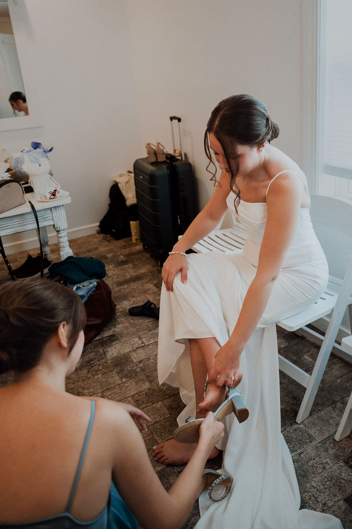 Chic bride sitting while bridesmaid helps put on shoes