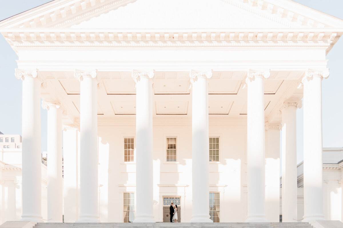 wide view of the virginia state capitol building close to sunset with a bride and groom standing face to face between the white columns