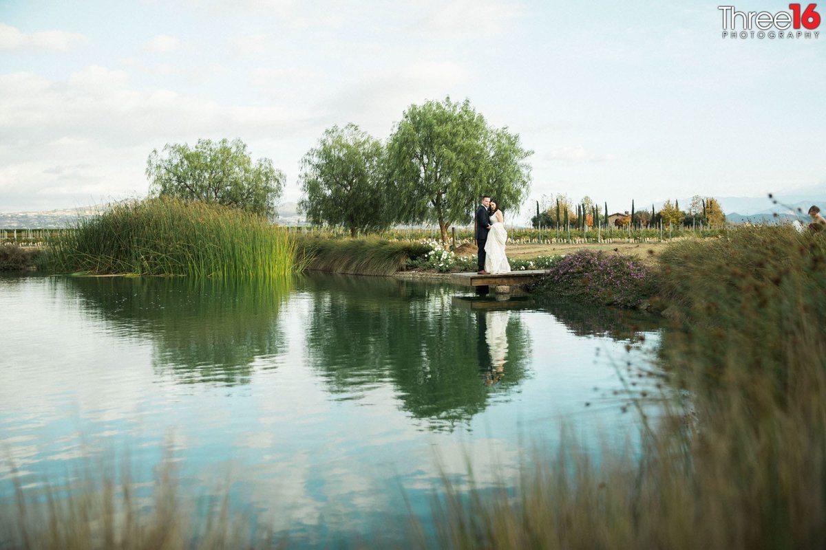 Bride and Groom pose together while standing on the end of a small dock overlooking a small lake