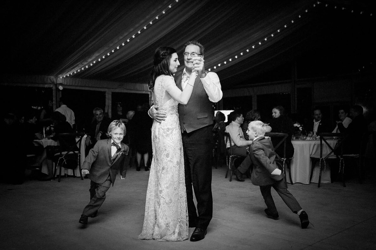 Heartwarming black and white photo of a bride dancing with an older man, two young boys dancing in the foreground.