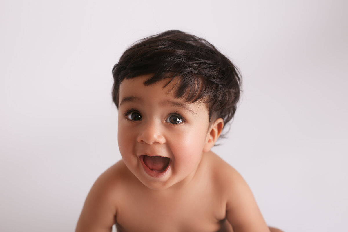 Head and shoulders of a happy six month old baby sitting on a white background.