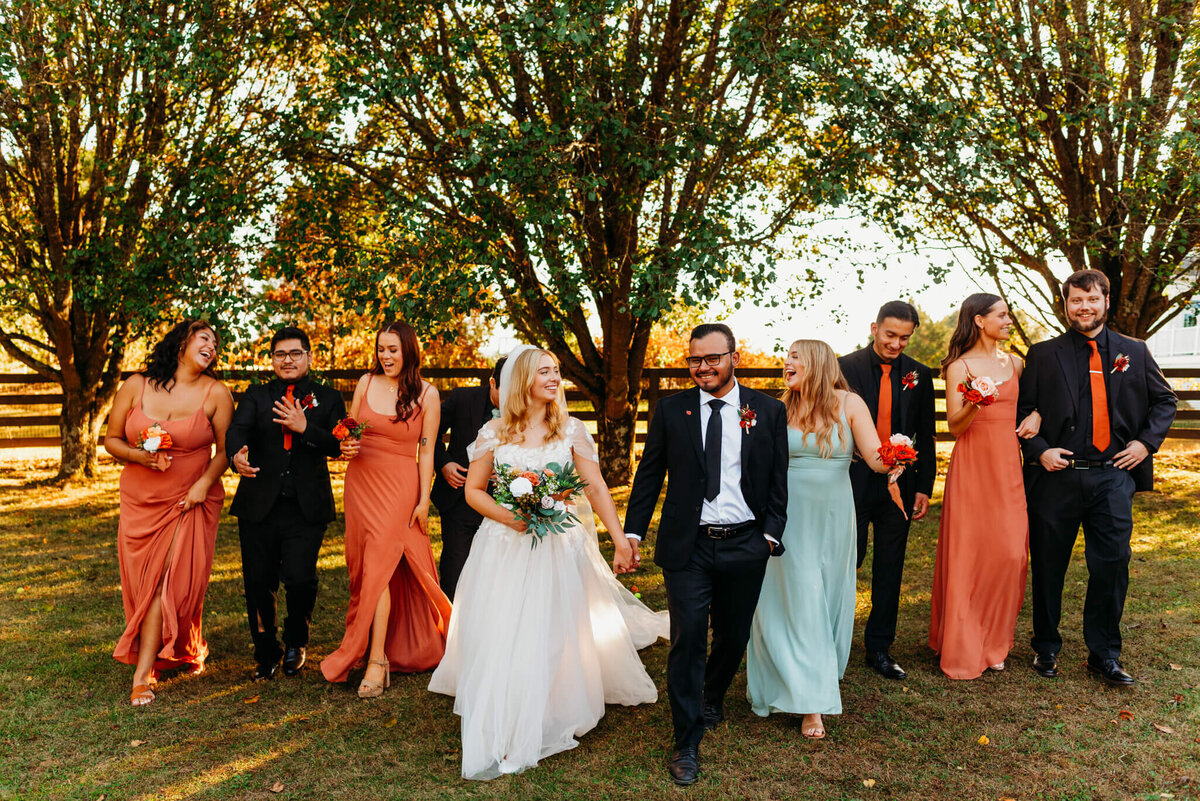 photo of a bride and groom holding hands and walking while the wedding party walks behind them