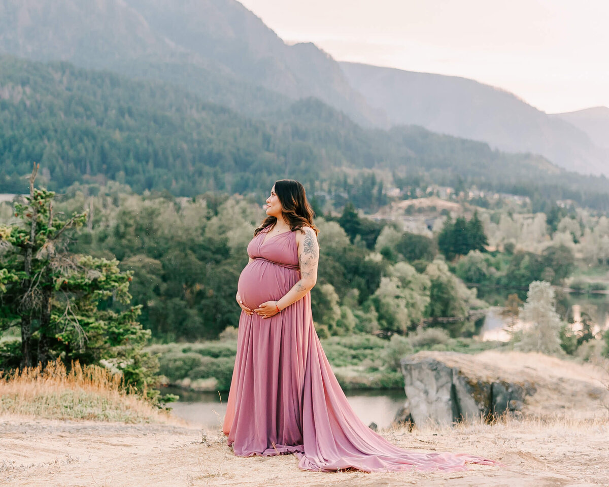mom wearing pink dress holding pregnant belly in maternity portrait in the columbia river gorge