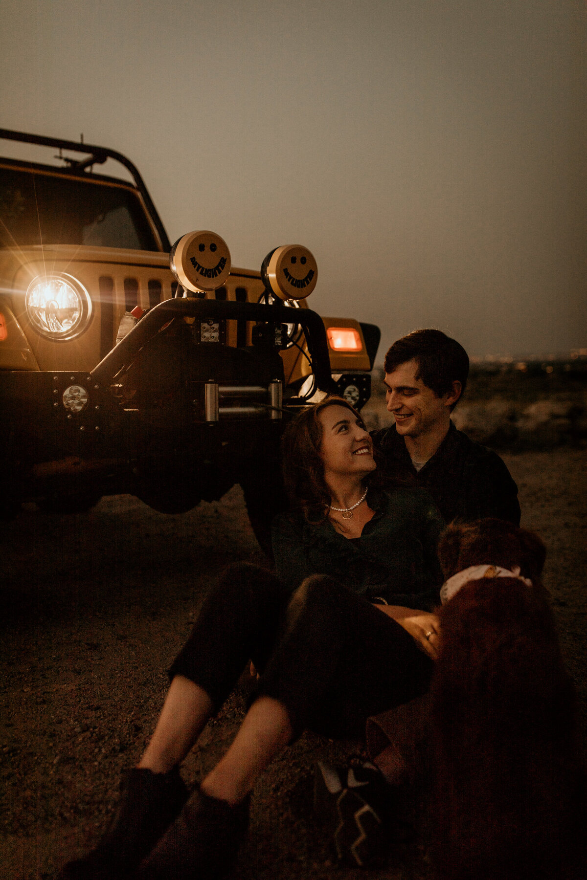engaged couple sitting in front of jeep at sunrise in Albuquerque