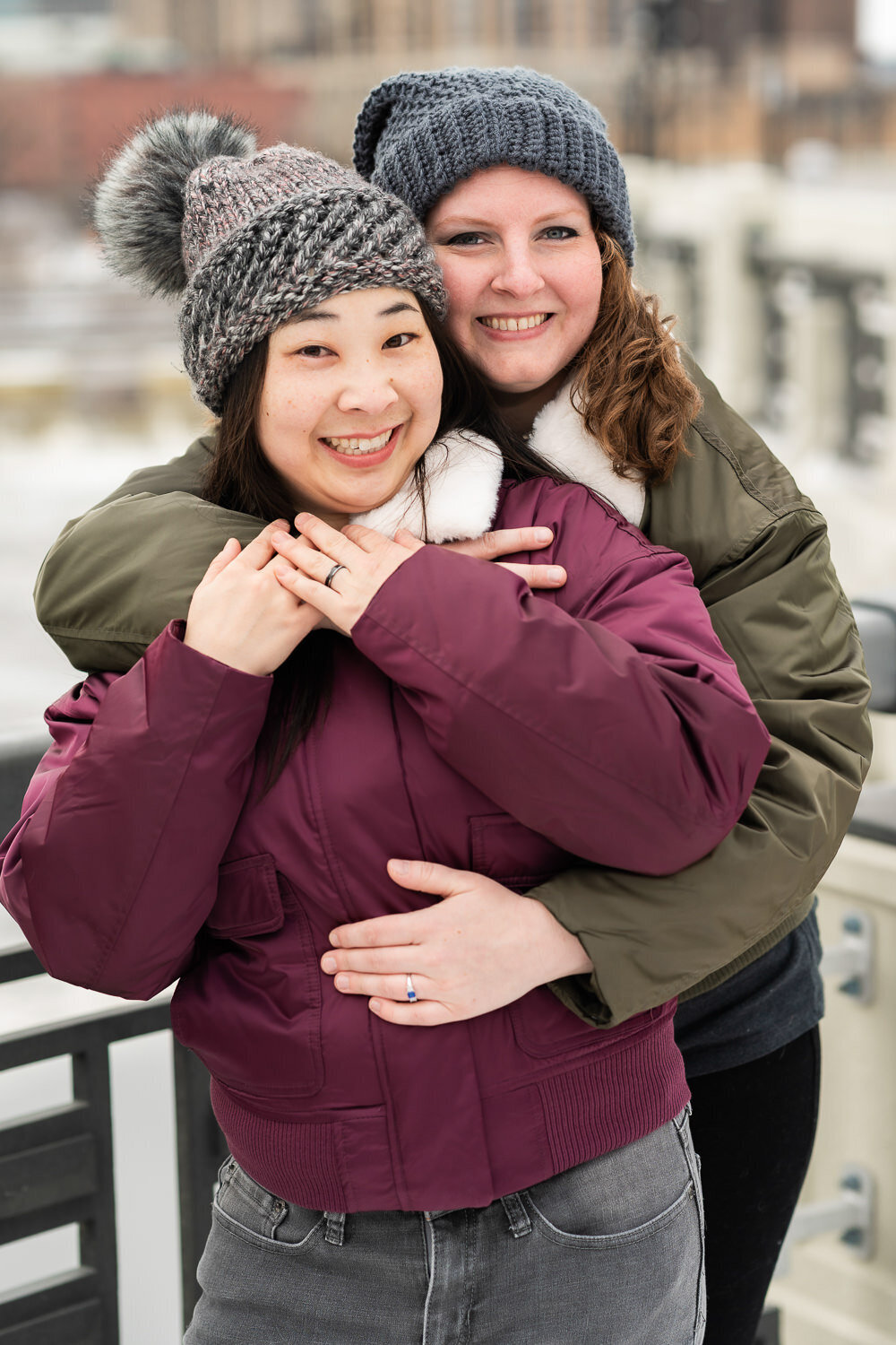 Lesbian couple wearing hats and jackets snuggle.