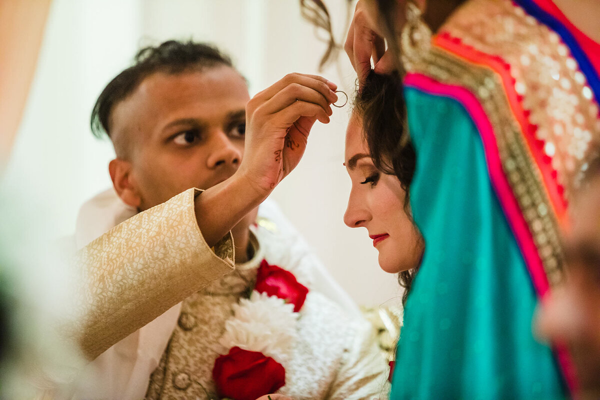 A groom adorns a bride's forehead with a traditional Indian 'sindoor' marking, symbolizing their marital bond.