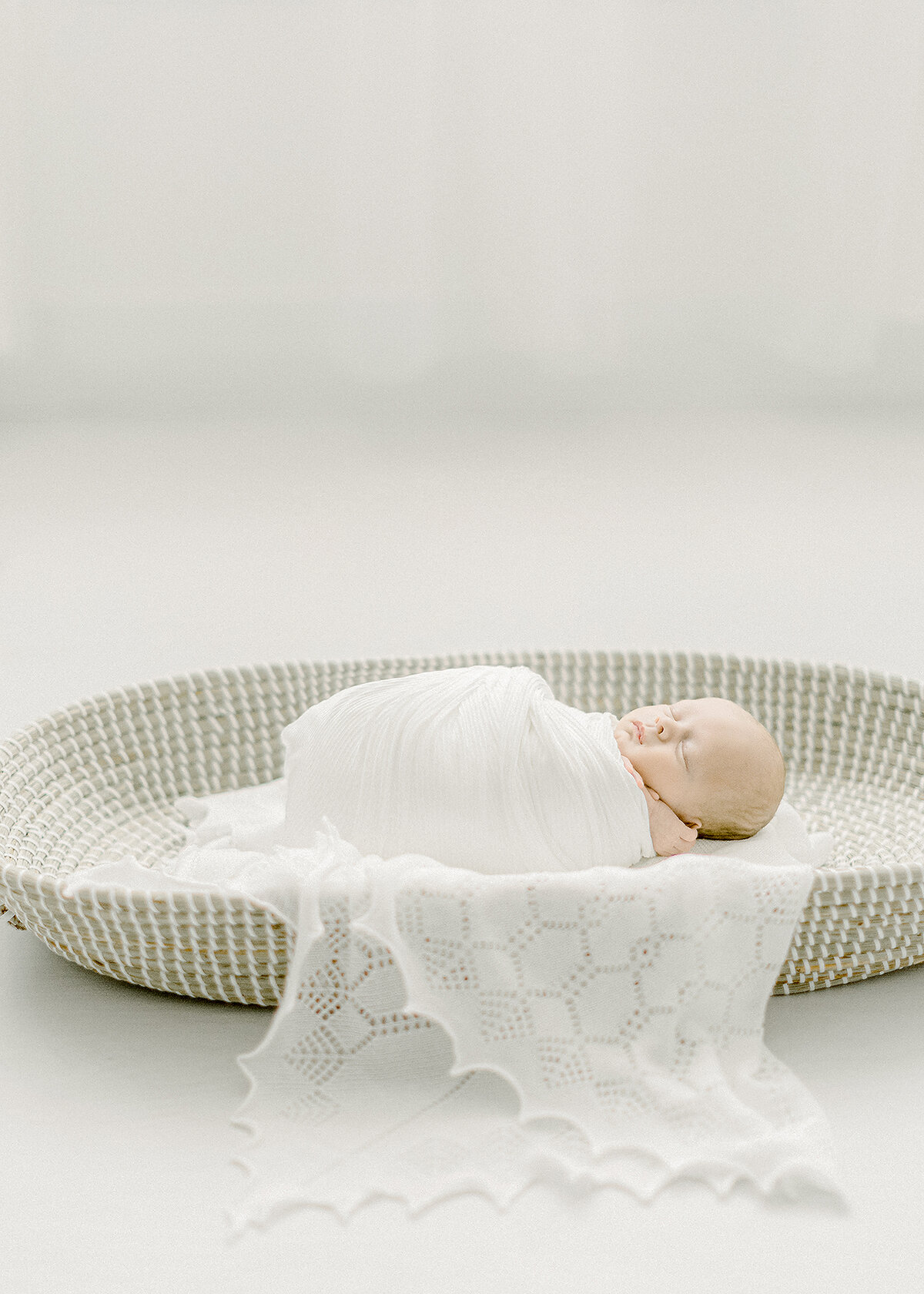 Newborn baby boy wrapped in a swaddle as he lays down in a basket on the floor at a Dallas TX photography studio.