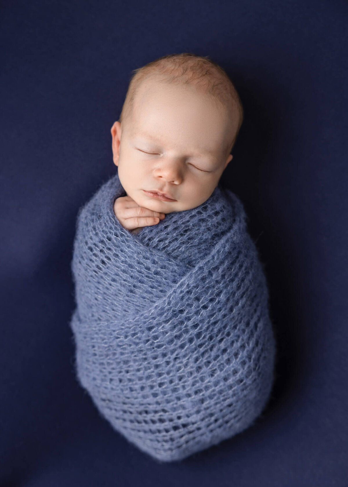 newborn baby asleep on blue fabric wrapped in blue knitted wrap