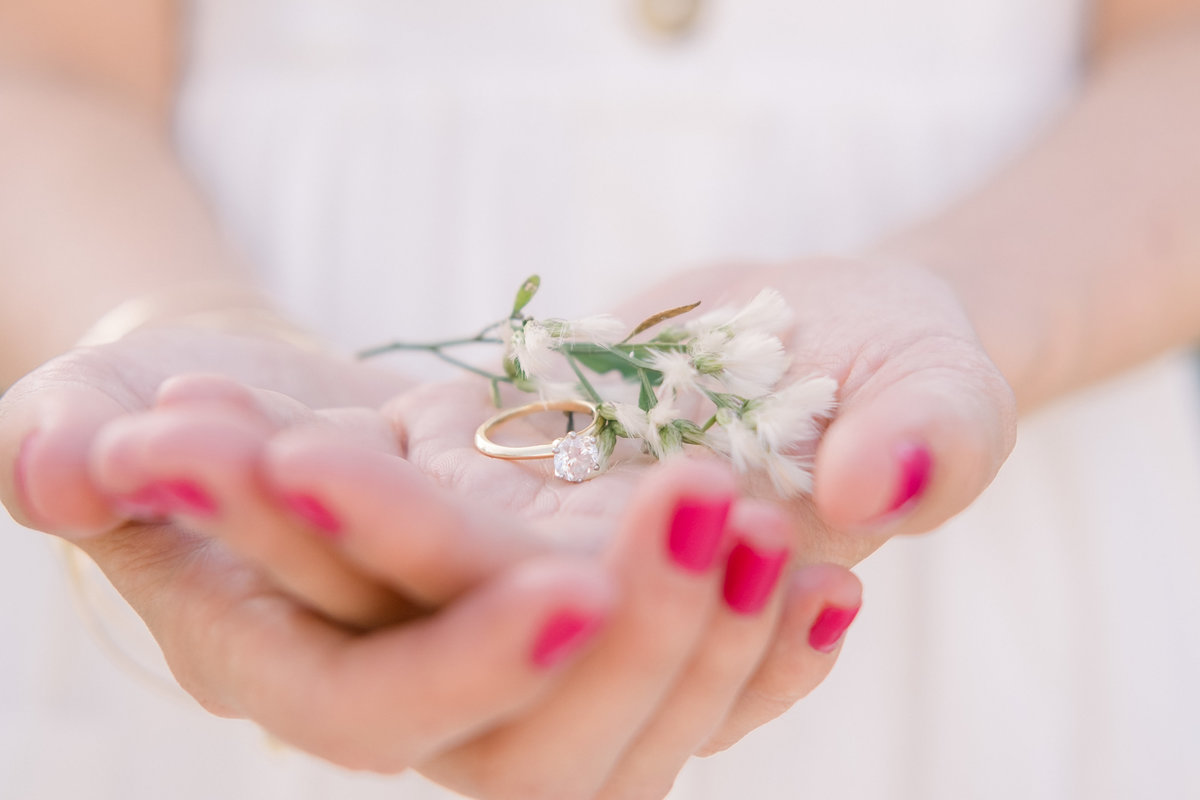 The hands of the bride to be holding her engagement ring with some simple white flowers