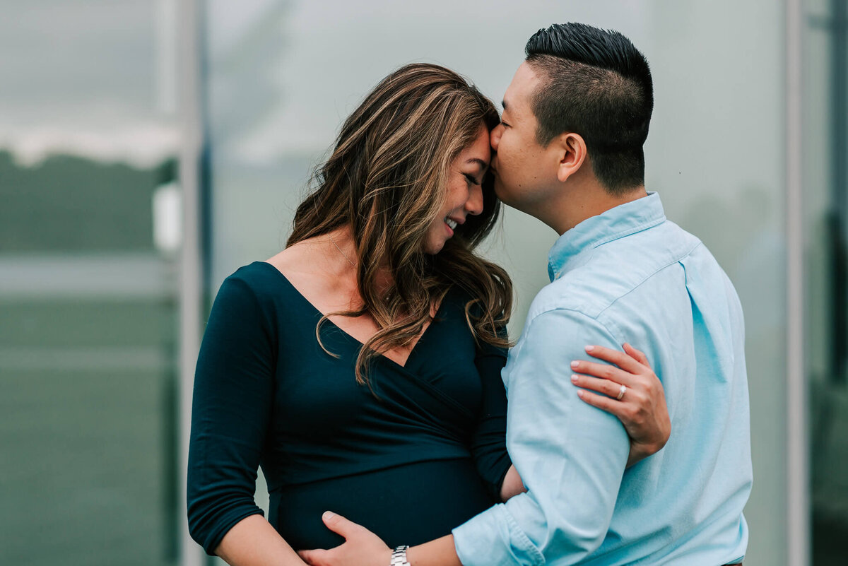 A man kisses his wife's forehead while holding her belly during their maternity session at the Kennedy Center