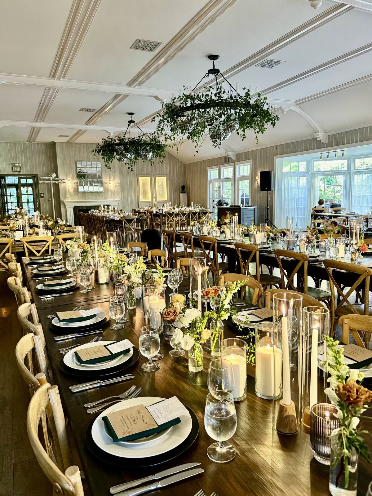 Long banquet table with greenery, candles, and place settings inside a warm, inviting reception space.