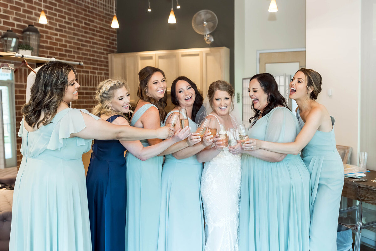 Bridal party in bridal suite at The Willows Event Center, Lubbock, TX wearing seafoam green and navy dresses and toasting with champagne