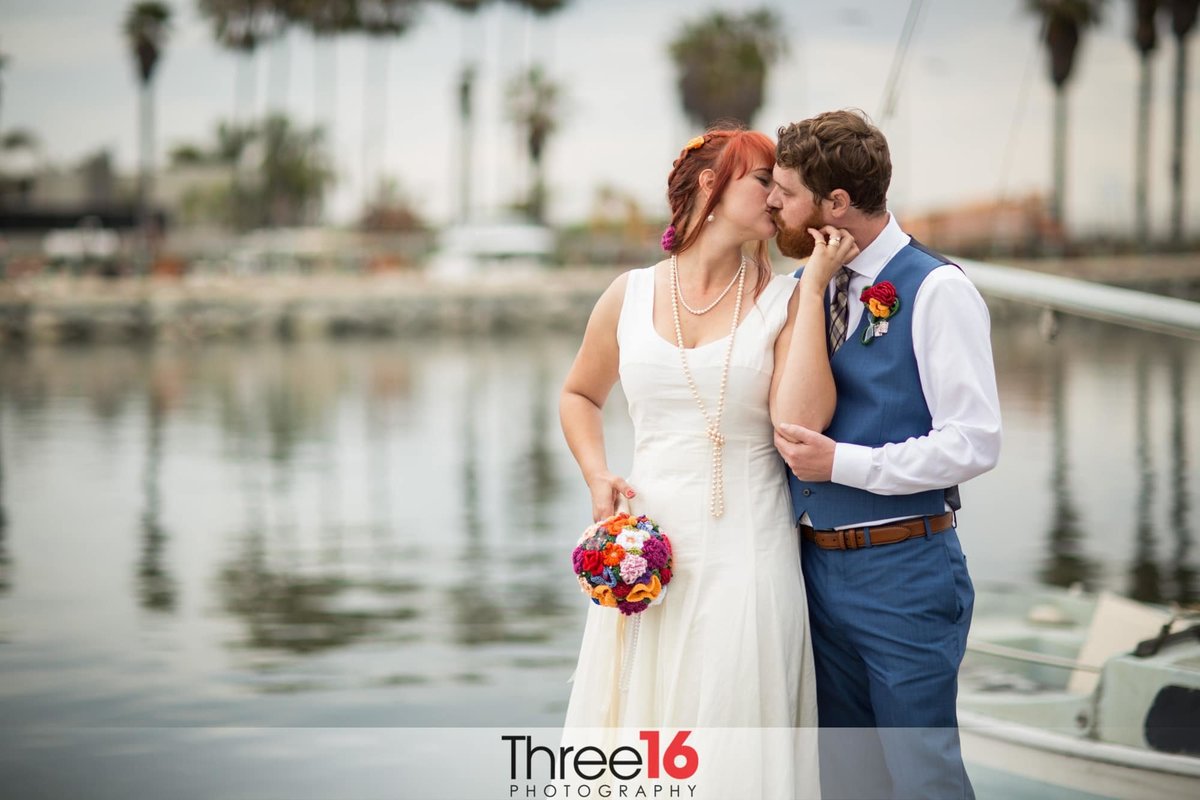 Bride looks back to her Groom as they share a romantic kiss standing on the docks at the Dana Point Yacht Club
