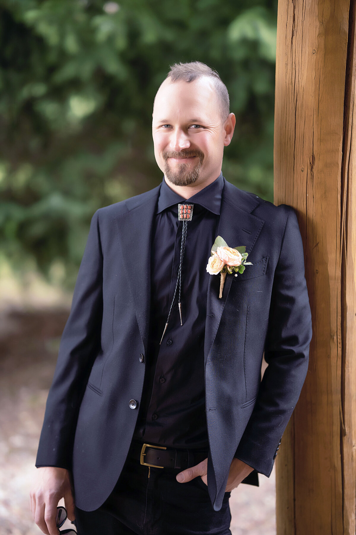 A handsome groom leans against a log cabin in Beyul Resort Aspen Colorado, getting ready for his wedding day.