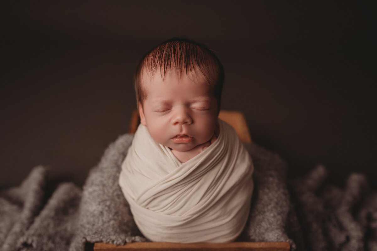 Atlanta newborn photography session with baby in cream swaddle posed sitting up in wooden basket