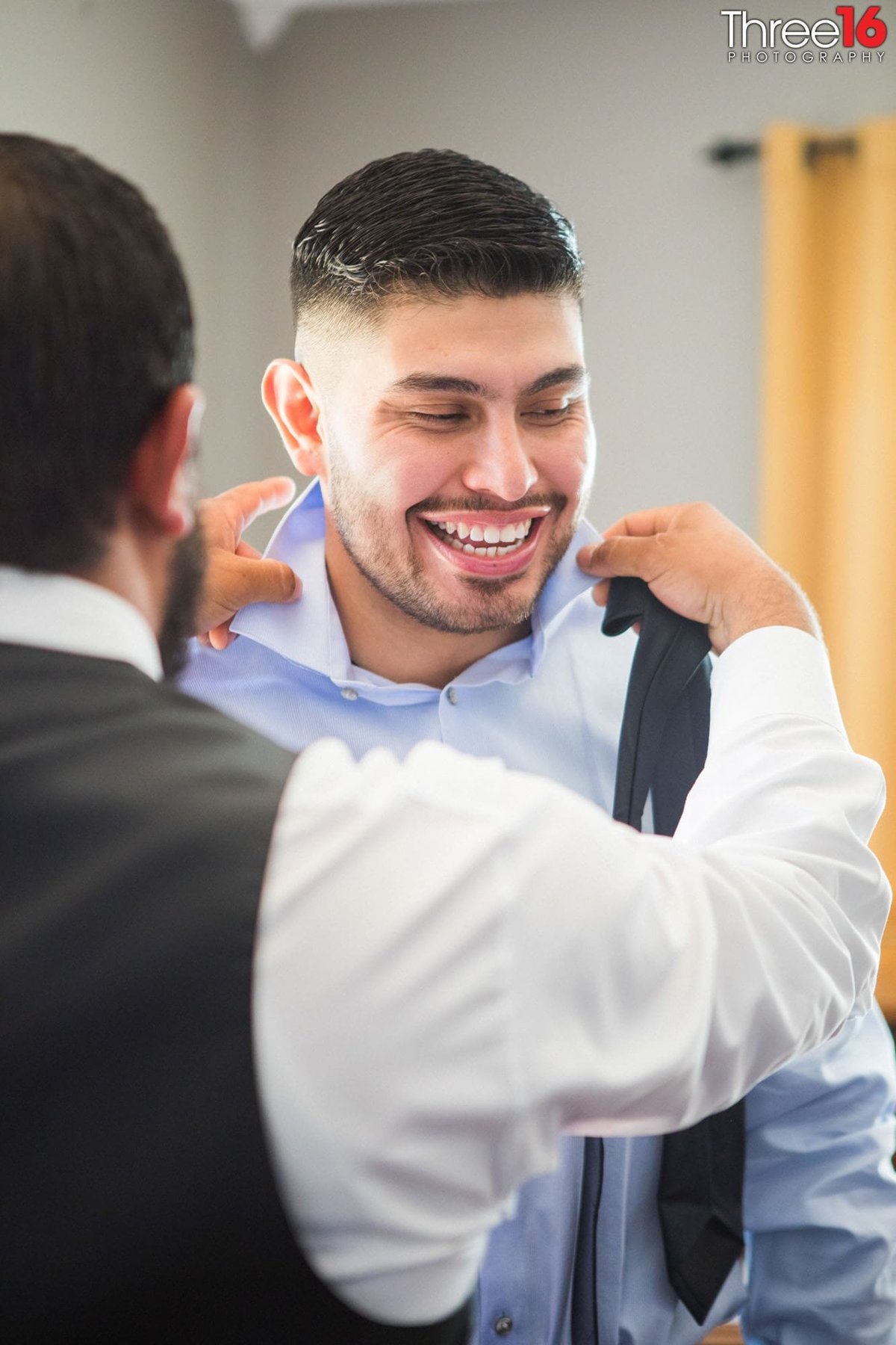 Groom getting help with his tie while getting ready for the wedding