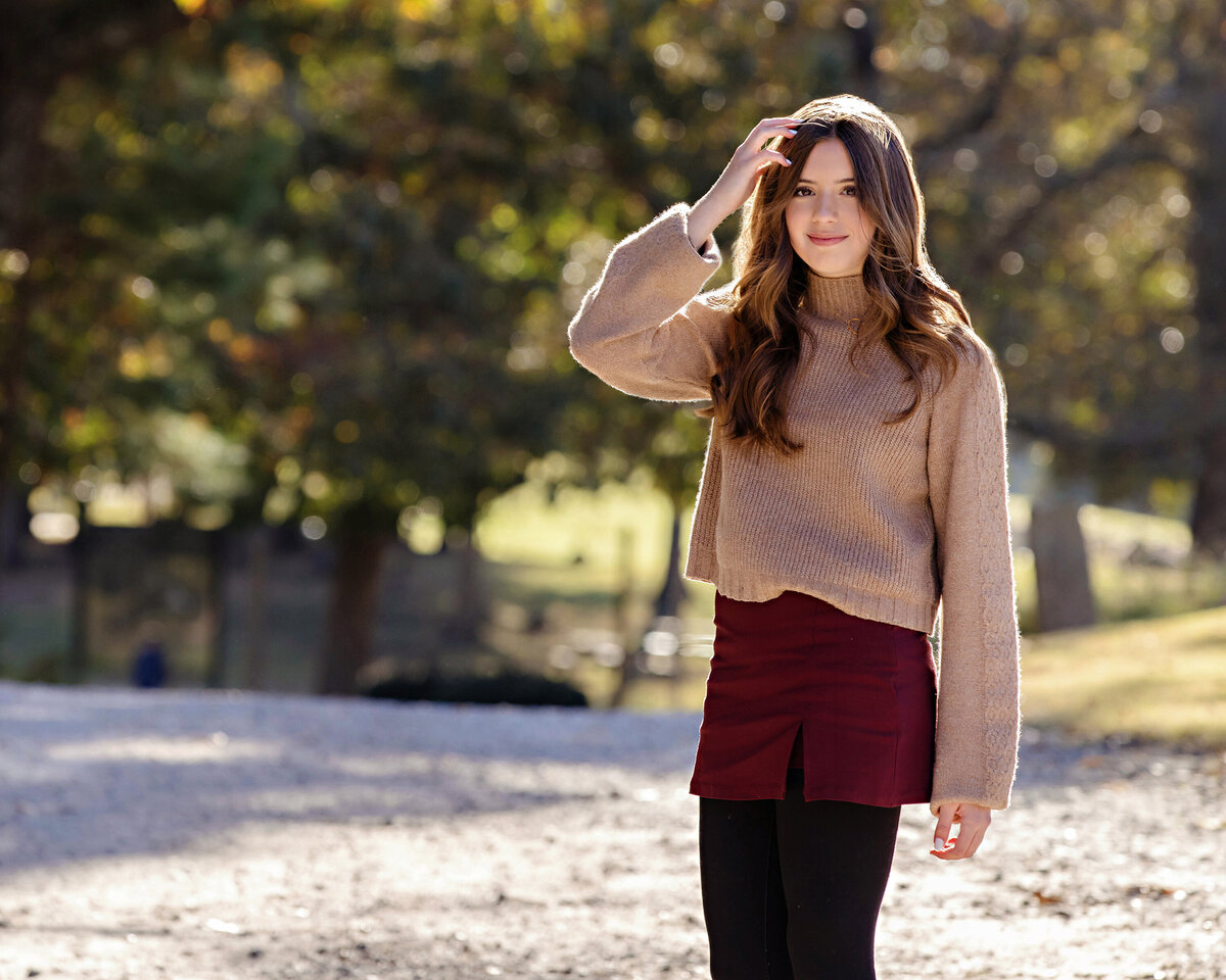 Charming young girl portrait in tan sweater on tree‑lined gravel road in autumn at Anne Springs Close Greenway