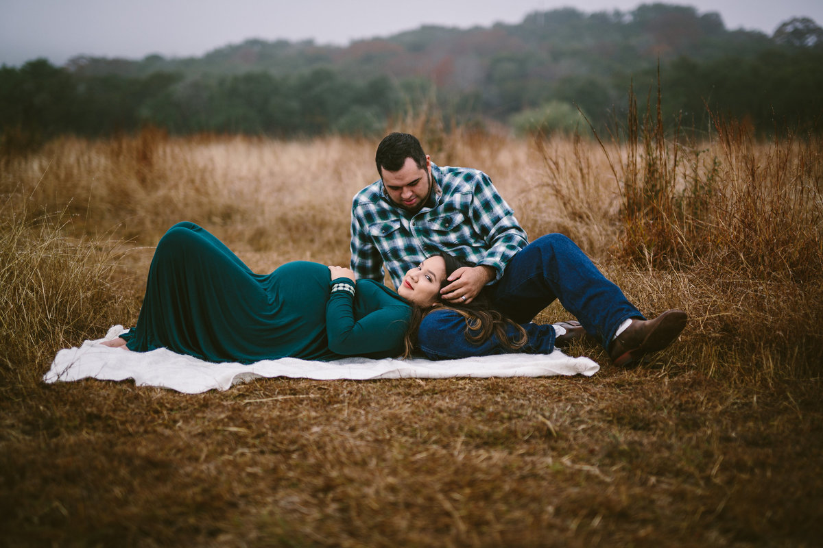 couple pregnant laying in open field in Texas hill country for their maternity session in Boerne
