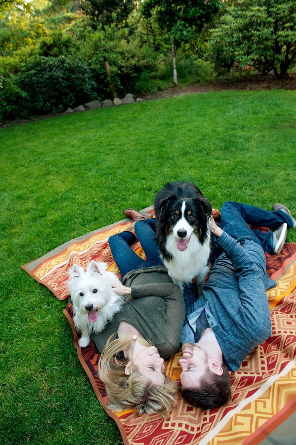 an engaged couple lay on a colorful blanket with their two dogs during their engagement session