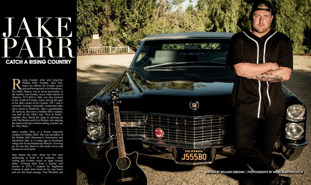 Magazine Article Publication Hidden Hills featuring country artist Jake Parr standing in front of vintage black care arms folded across his chest guitar leaning on bumper beside him