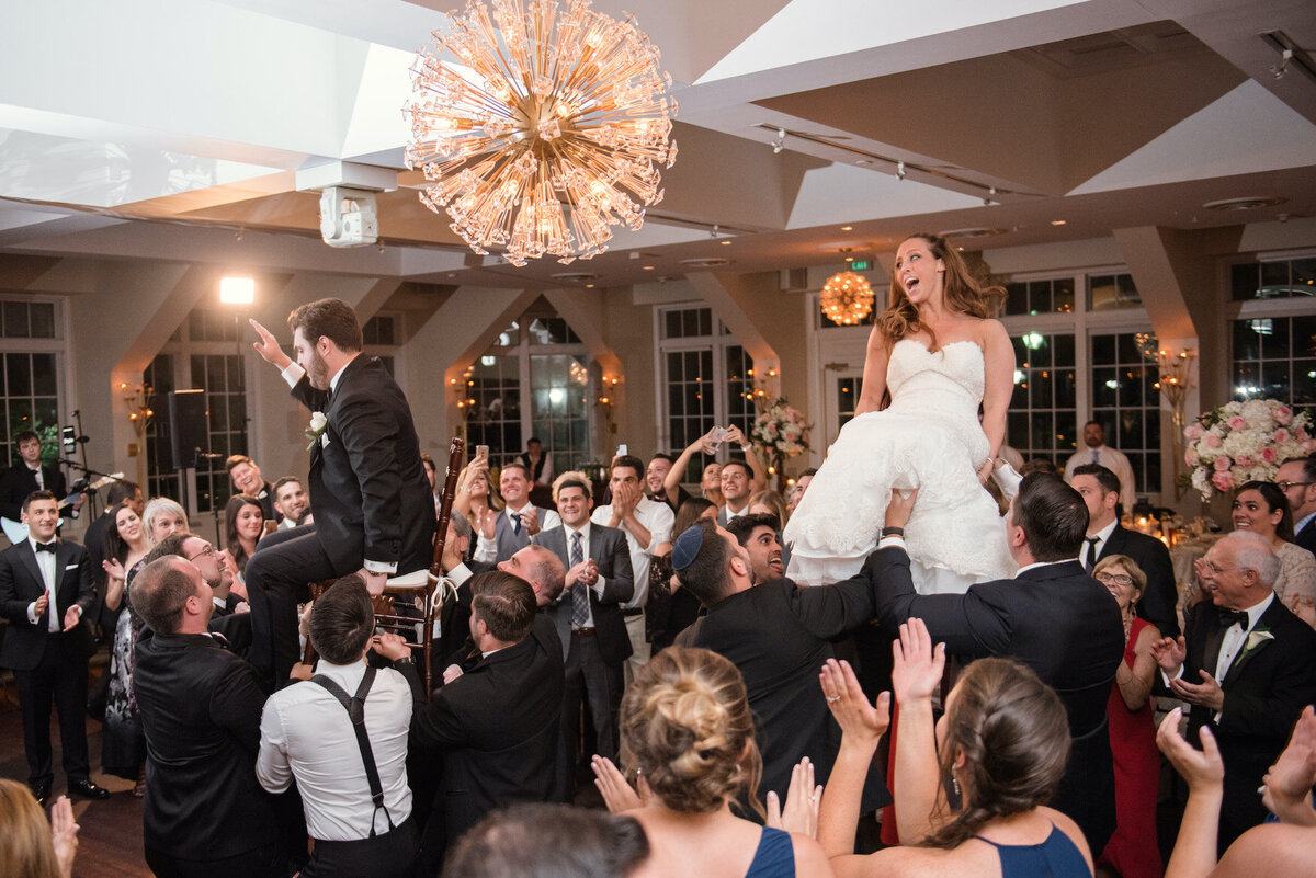 bride and groom on chairs during the horah at Heritage Club at Bethpage