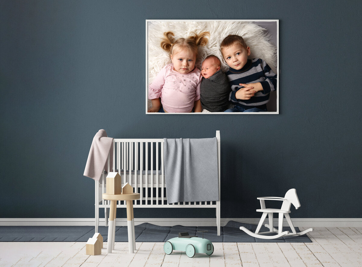 Large print of newborn and two siblings on a blue wall in nursery