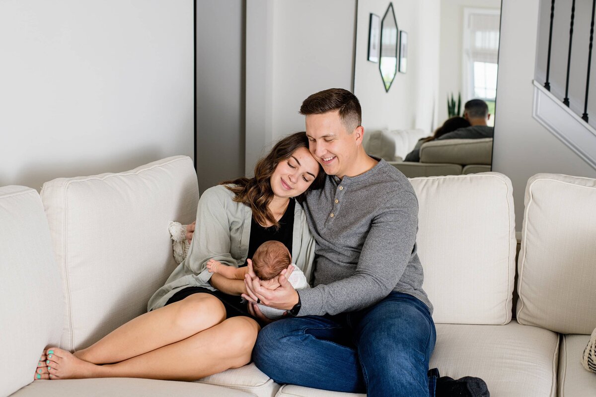 family of three sits on their charlotte area home sofa while cuddliing their newborn daughter